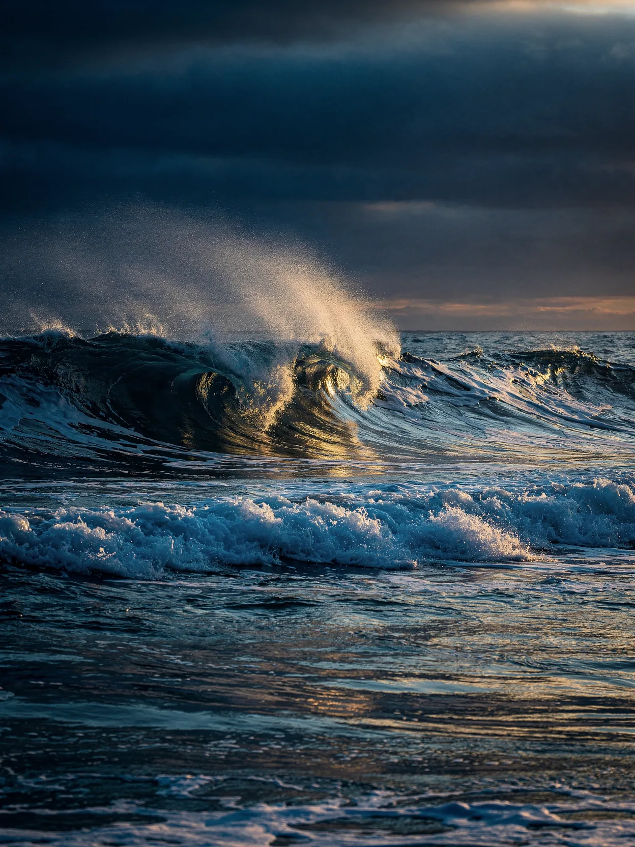 A dark blue wave breaking at dusk